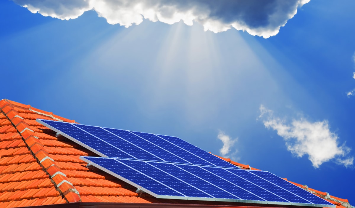 l'immagine ricorda una nuova era nel mercato fotovoltaico grazie al credito di imposta. Si vede il sole dietro le nuvole che illumina i pannelli solari su un tetto di una casa.